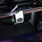 Close-up view of a 3D printer extruder head inside a 3D printing machine.