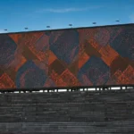 Large outdoor digital billboard displaying an abstract red and blue geometric pattern against a blue sky.