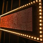 A horizontal marquee sign with orange lights and bulbs, photographed from an angled side view at night.